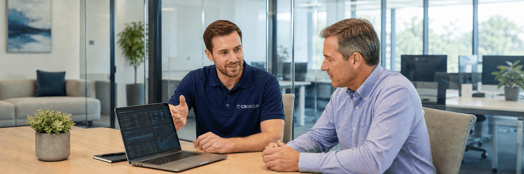 C9 GROUP staff member in navy polo explaining network security to a business owner on a laptop